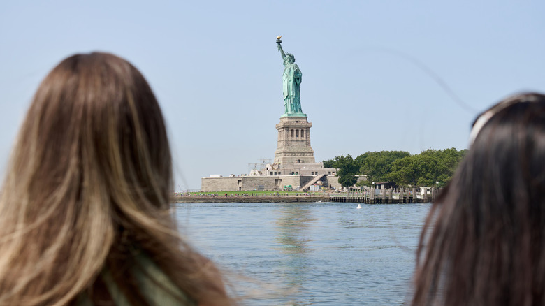 Two tourists admiring the Statue of Liberty from a ferry.