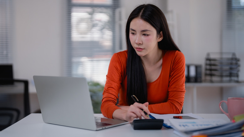 A young woman making financial calculations with a laptop and a calculator