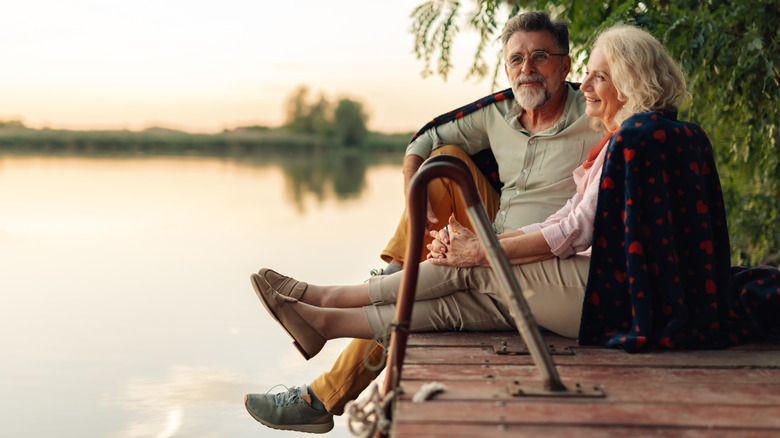 a retirement age couple sits on a dock looking at a lake