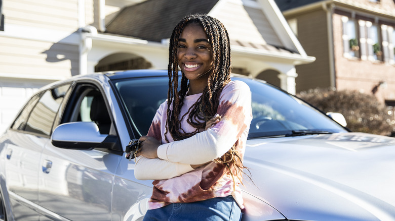 Smiling teenager standing in front of a silver car