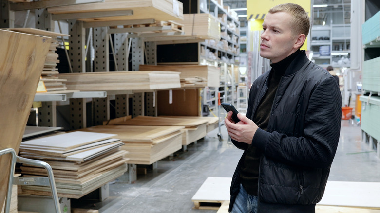 Man holding smartphone while shopping for wood