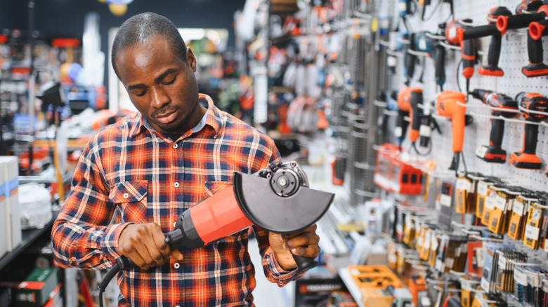A male shopper in a flannel shirt looks at a power tool in a hardware store