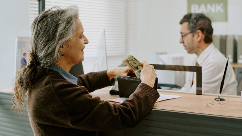 Elderly woman taking cash from a bank teller and putting it in her purse