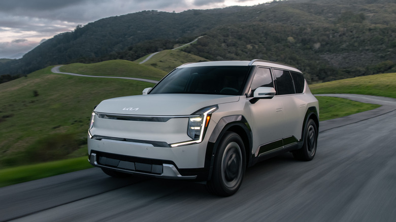 a 2024 Kia EV9 on a curvy mountain road with tree-covered mountains in the background