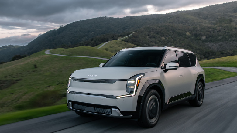 a 2024 Kia EV9 on a curvy mountain road with tree-covered mountains in the background