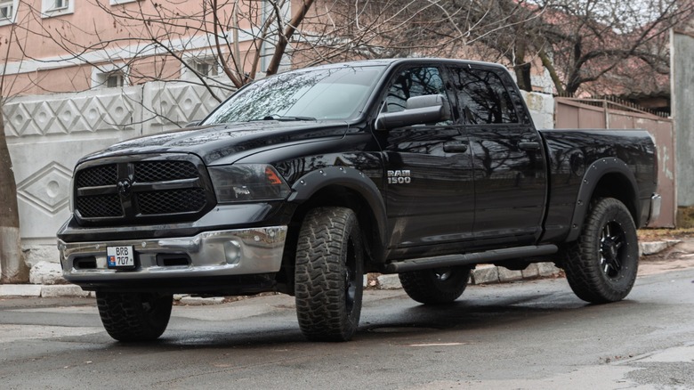 Black Ram 1500 pickup truck parked on a residential street, featuring off-road tires and a chrome front bumper