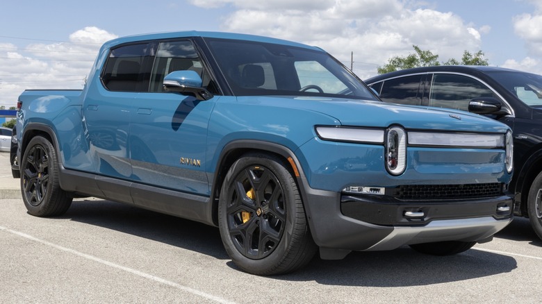 Blue Rivian R1T electric pickup truck parked in a lot, featuring distinctive oval LED headlights and black wheels