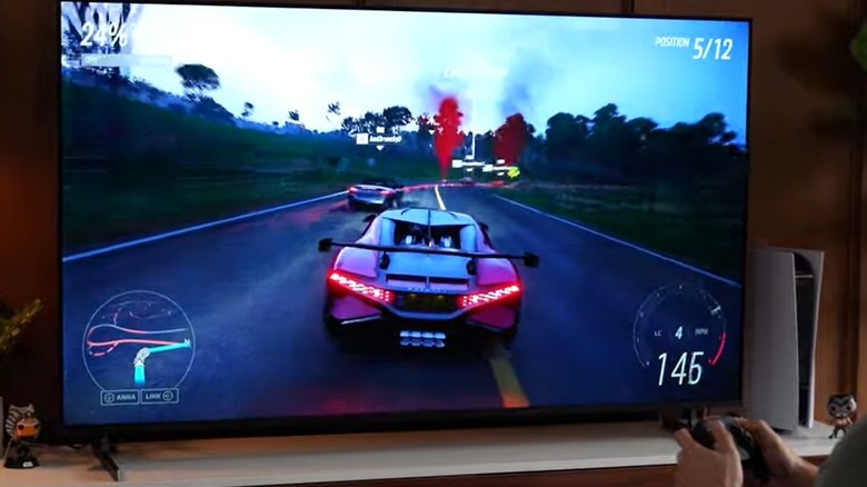 Racing video game on smart TV screen, man's hands holding game remote in bottom right corner