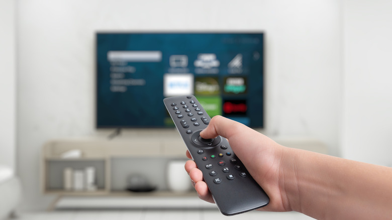 Hand aiming a remote at smart TV blurred in background