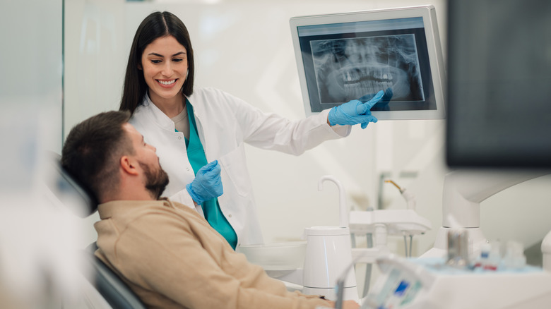 A dentist explaining an x-ray shown on an overhead screen to a patient in the dentist's chair.