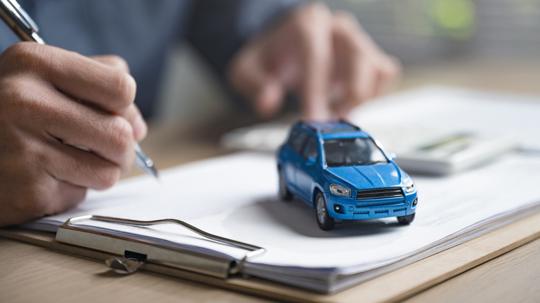 A man writing on a piece of paper with a blue toy car on the paper