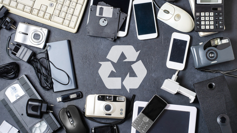 Various types of outdated electronic devices around recycling sign