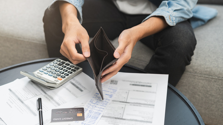 A man holding an empty wallet and a credit card bill