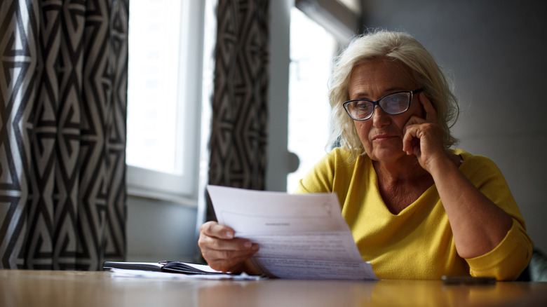 Older woman looking over paperwork while seated at a table.