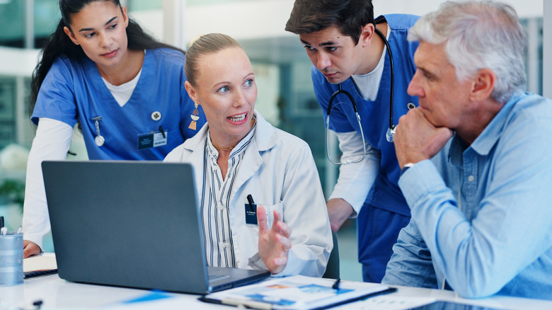 A medical team huddled around a laptop discussing something with a mature male patient.