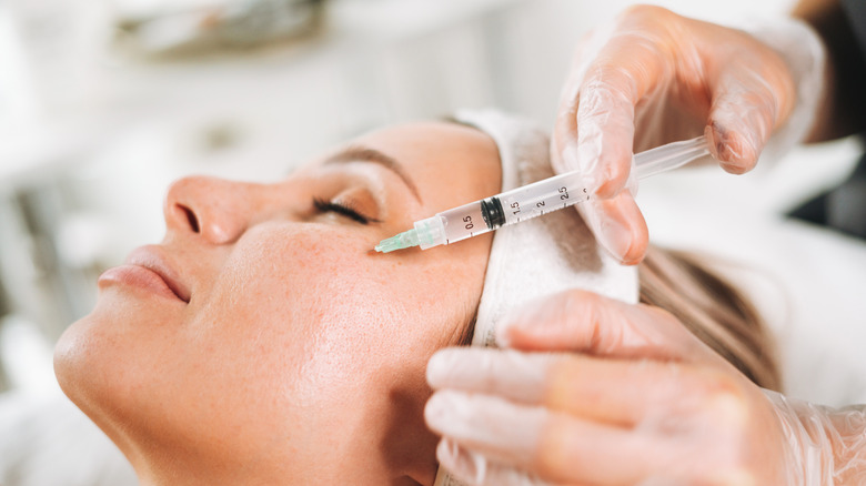 A woman getting cosmetic injections in her face while lying on couch in beauty salon