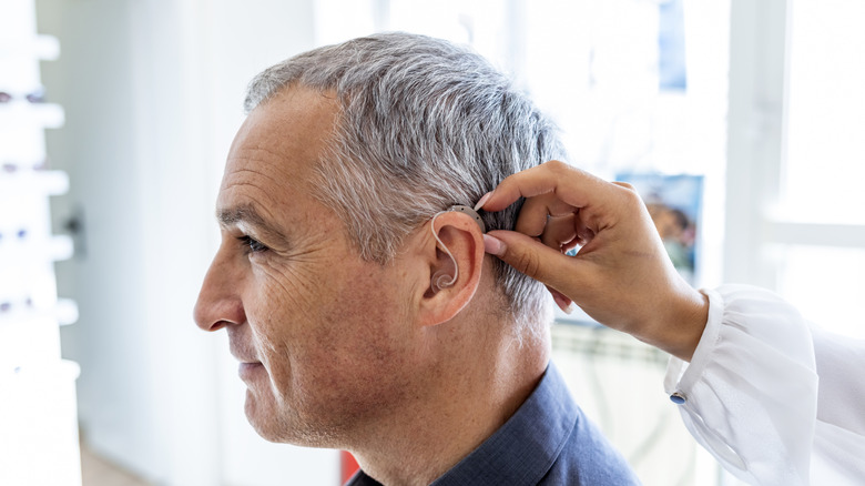 A hearing specialist placing a hearing aid in a mature man's ear.
