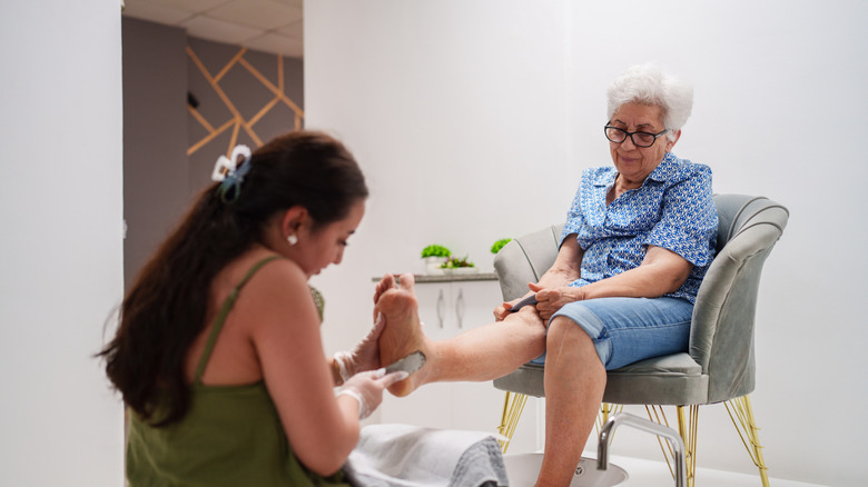 A caregiver giving a seated elderly woman a foot exfoliation and pedicure.
