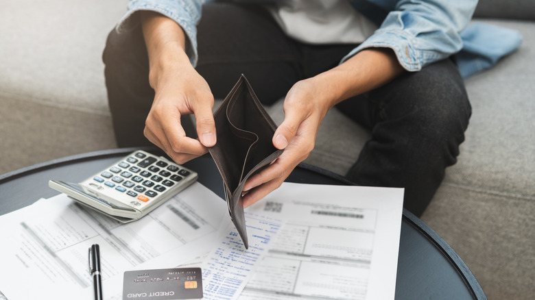 man holding empty wallet and looking at credit card bills
