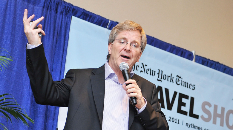 Rick Steves gestures while speaking into a microphone on stage
