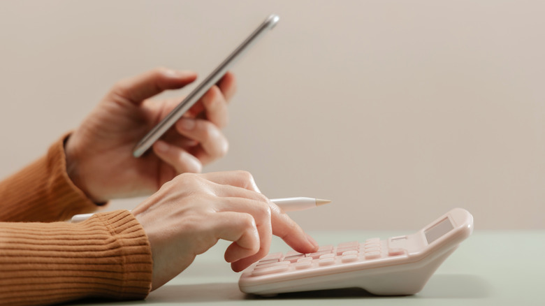 Person using a calculator and holding a phone