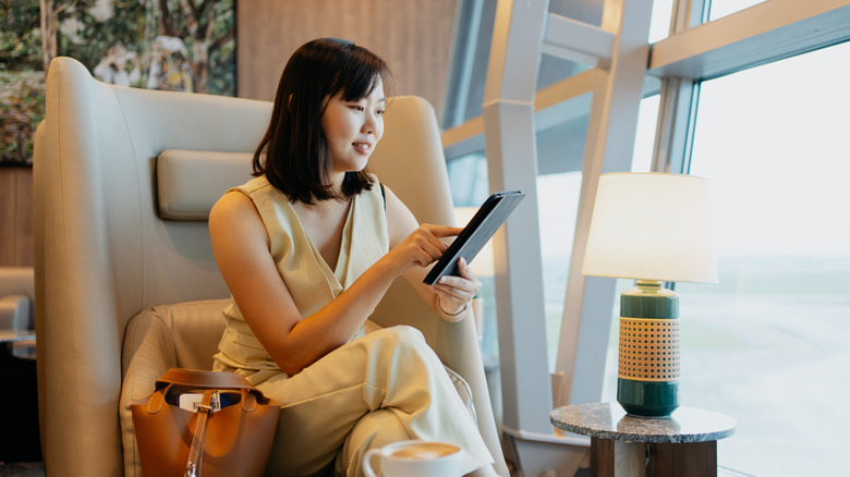 A businesswoman using digital tablet while waiting for flight at airport lounge.