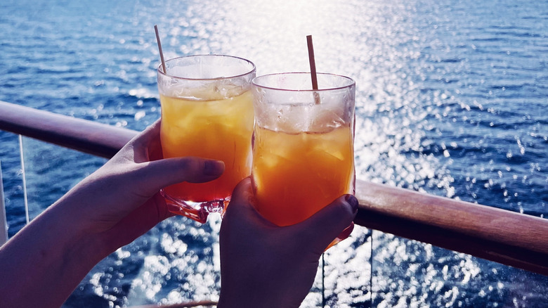 Two people cheering drinks while looking out over the side of a cruise ship at the ocean.