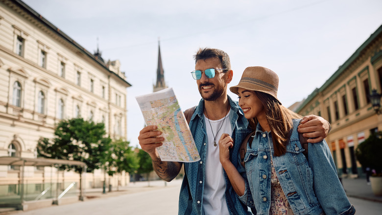 Happy couple of tourists reading map while walking through the city.