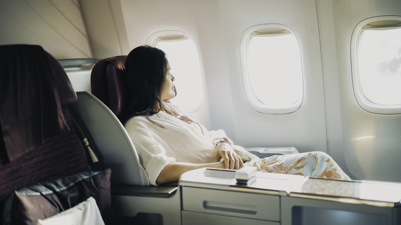 A relaxed business class passenger is looking out of the window of a passenger aircraft.