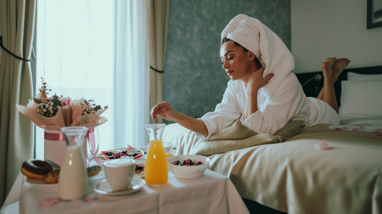 A young woman wearing a bathrobe and a towel after a morning shower eating a room service breakfast in a hotel room.