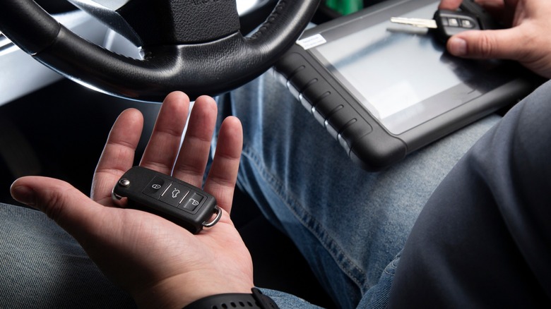 Man setting up and programming keys while holding a key fob behind a steering wheel