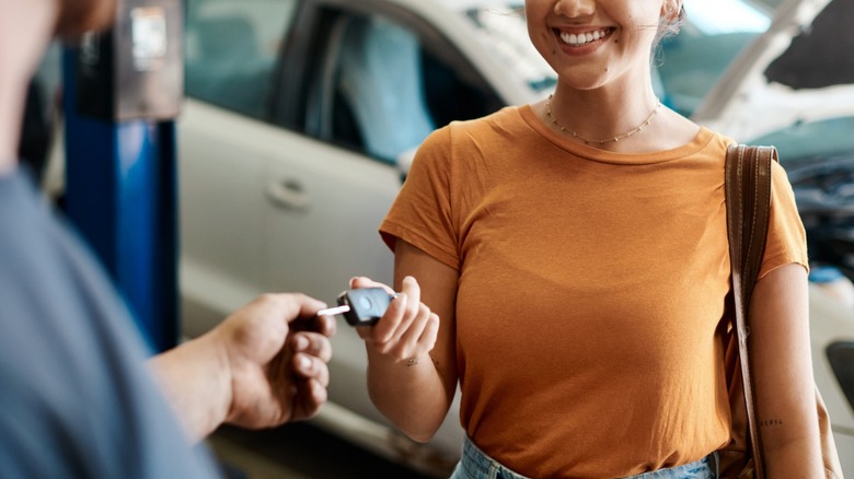 Woman in an orange shirt receiving a key to a car at a dealership