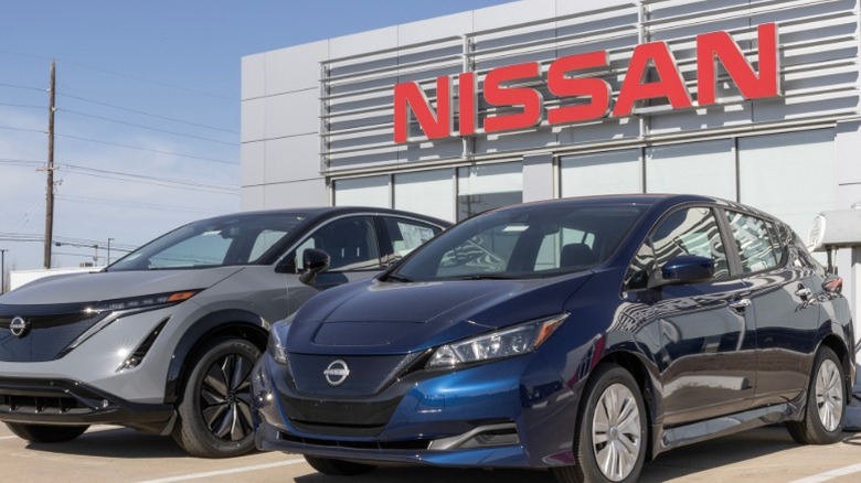 A blue Nissan Leaf car parked outside of a Nissan dealership next to another Nissan vehicle.