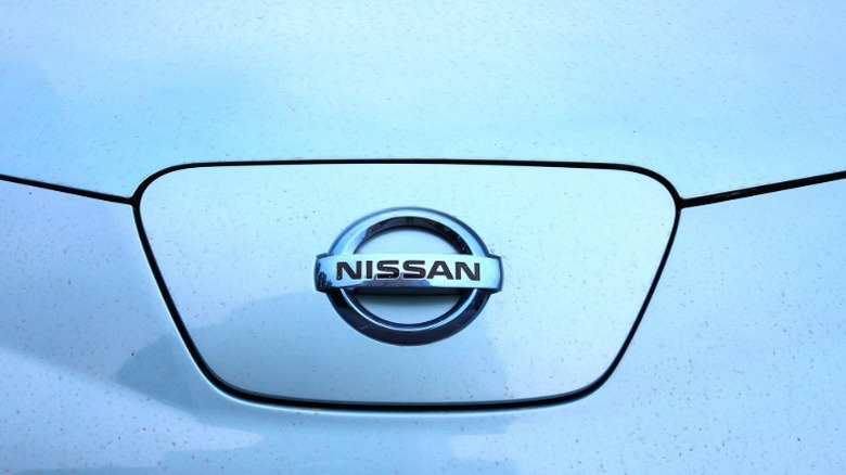 The front of a light blue Nissan Leaf showing only the Nissan emblem.