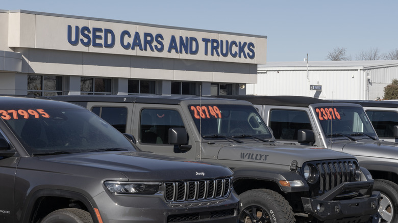 A used car dealership with preowned SUVs displaying prices in orange on their windshields.