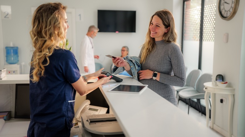 Smiling woman at clinic paying for medical treatment with a card.