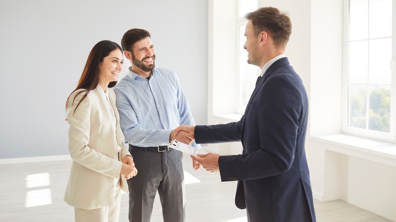 Family couple shakes hands with a real estate agent or realtor, sealing an agreement on a new home purchase