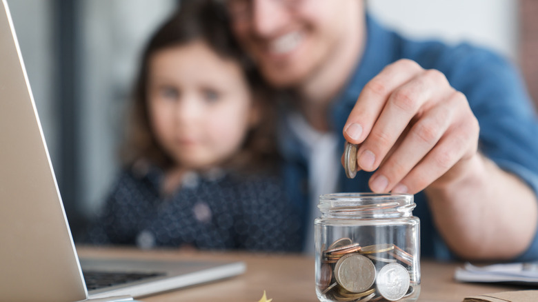 Father and daughter saving coins in a jar