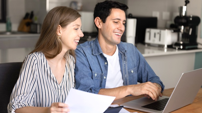 Smiling couple viewing laptop and papers