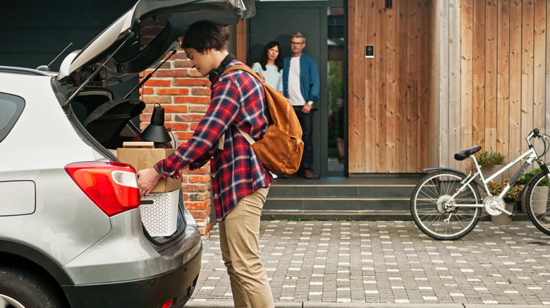 Teen boy packing up car with parents standing in doorway